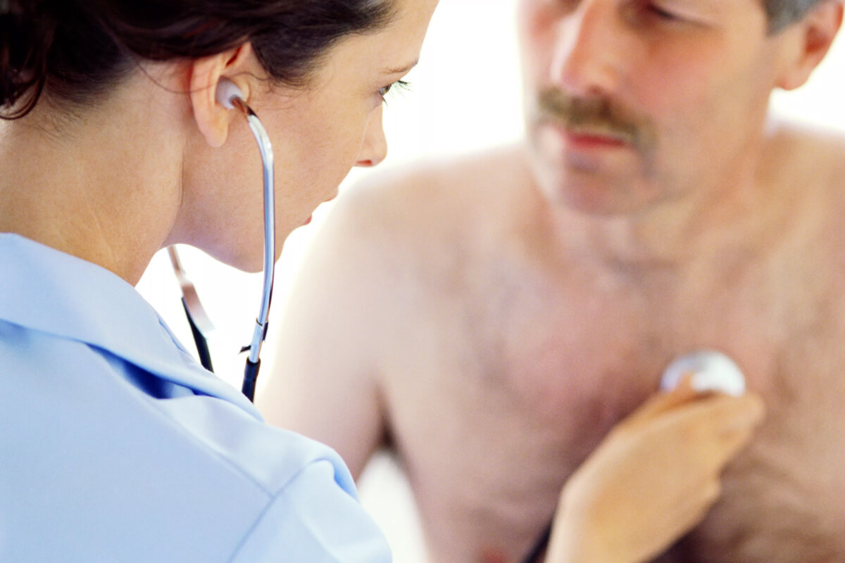 Врач-кардиолог слушает сердце у мужчины с усами